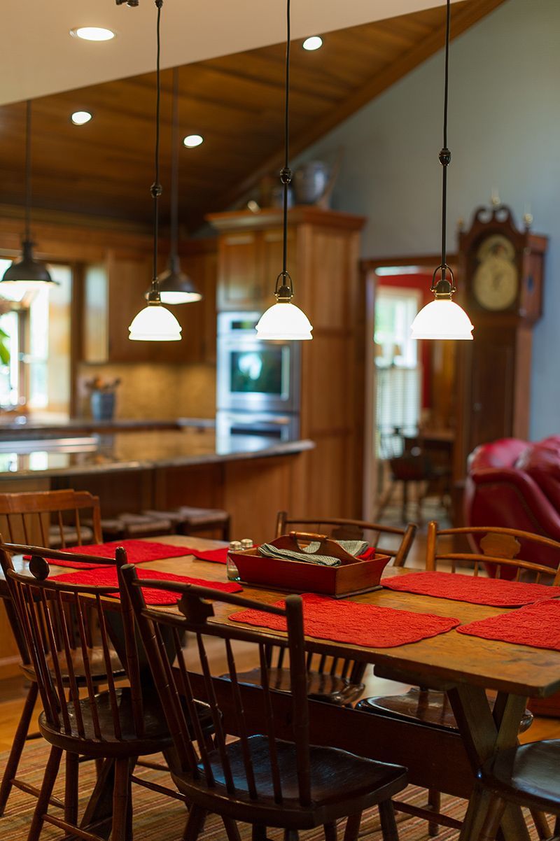 Dining room with wooden table, red placemats, pendant lights, open to a kitchen with cabinets.