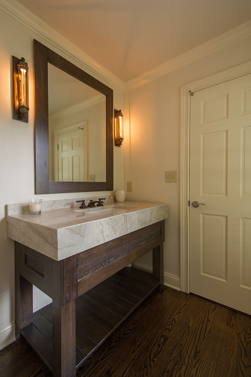 Bathroom with wood vanity, marble countertop, mirror, sconces, and closed white door.