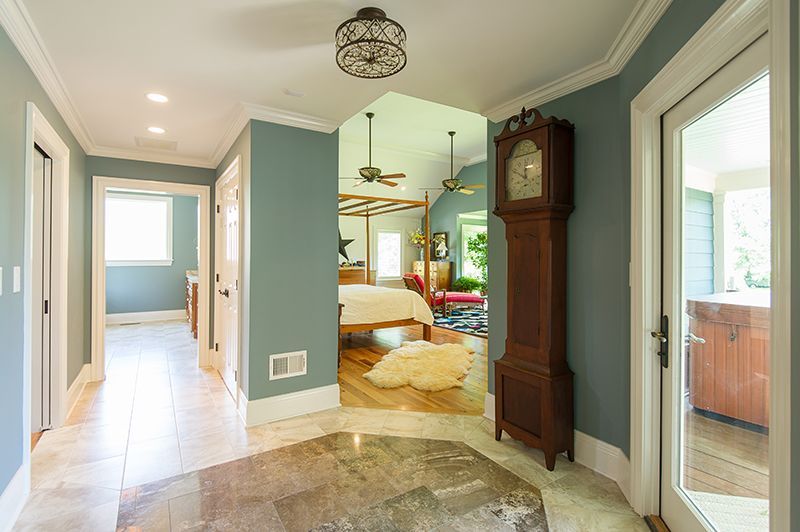 Hallway with blue walls, marble floor, grandfather clock, leading to bedroom with four-poster bed.