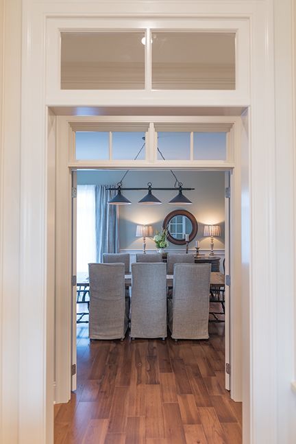 Open doorway to a dining room with a long table, chairs, and a circular mirror.