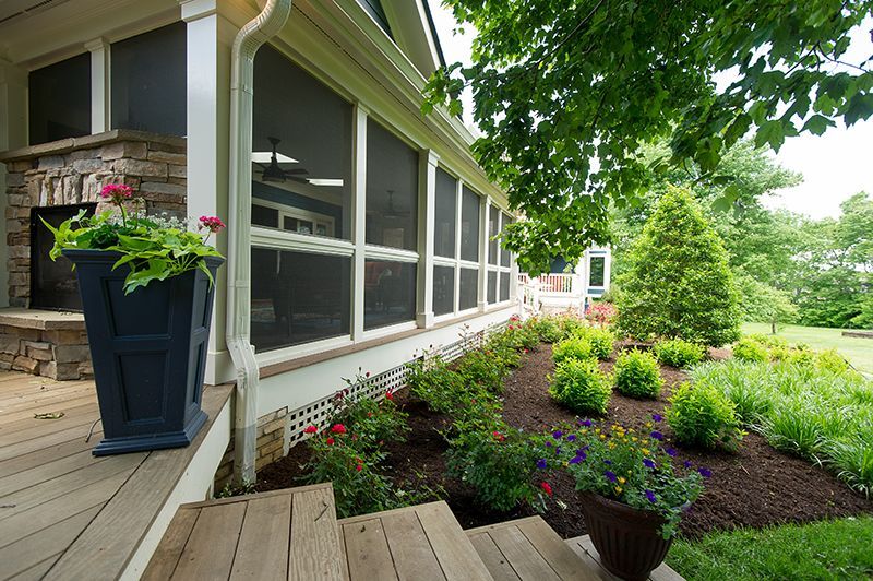 Screened porch with wooden steps, stone fireplace, and manicured garden.