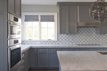 Gray kitchen with stainless steel appliances, gray cabinets, patterned backsplash, and a window.