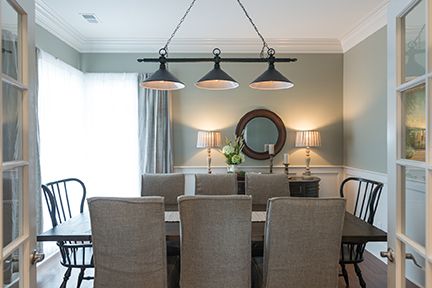 Dining room with long dark table, upholstered chairs, hanging lights, and a mirror.