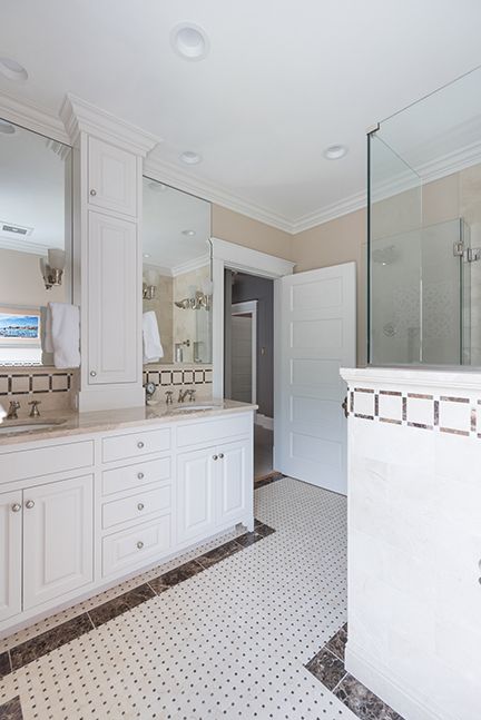 White bathroom with double vanity, patterned tile floor, and a glass shower.