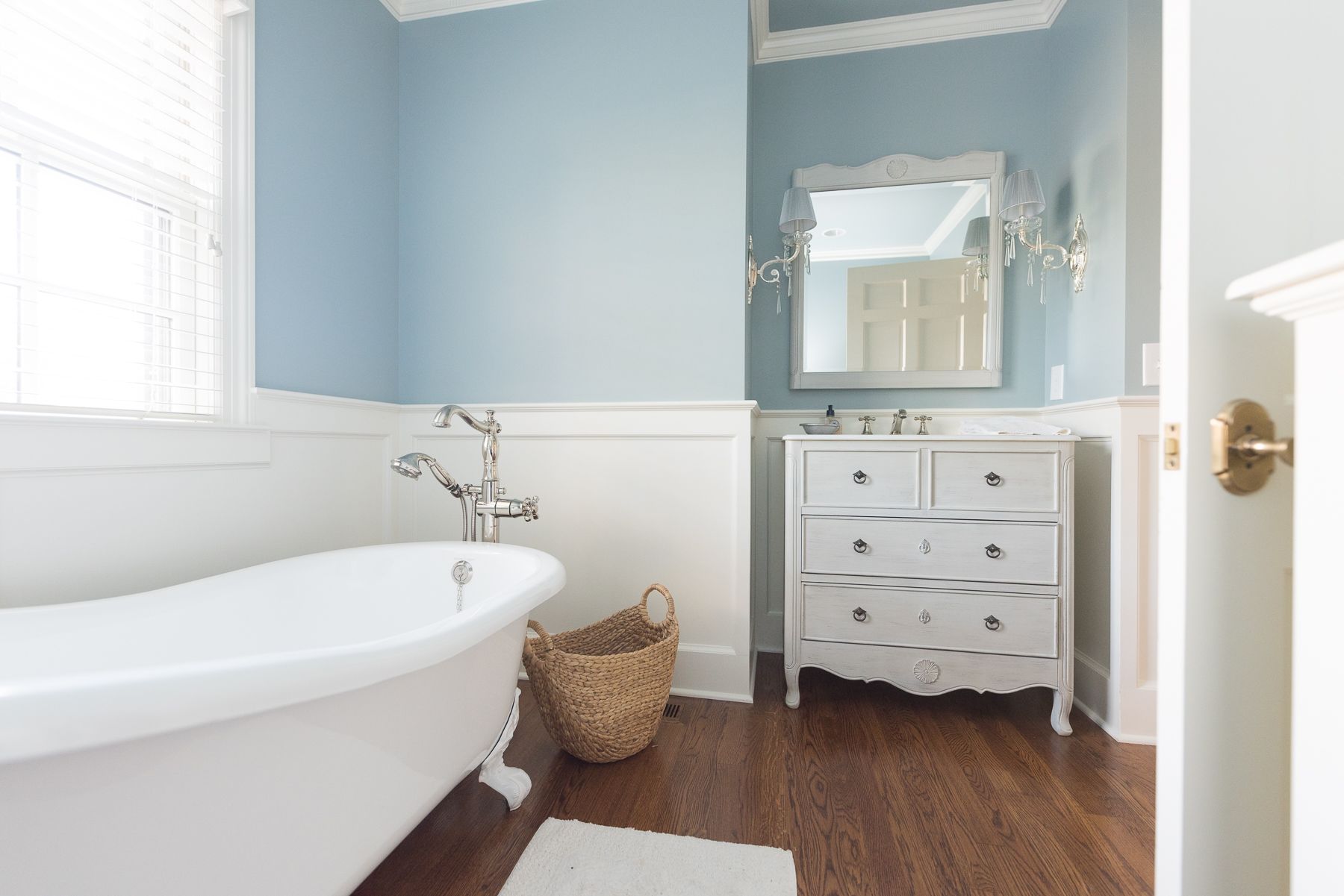 Bathroom with a white clawfoot tub, white vanity, light blue walls, and dark wood floor.