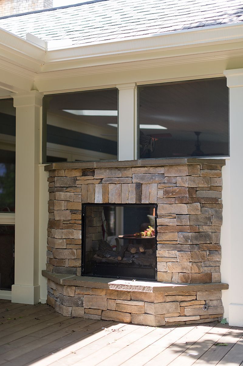 Stone fireplace on a wooden deck under a roof with two windows, fire burning inside.