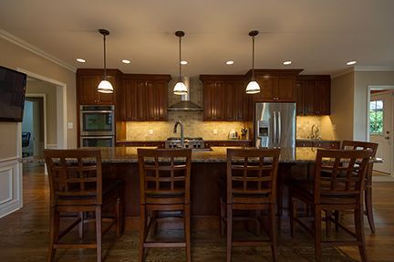 Kitchen with wooden cabinets, granite countertops, stainless steel appliances, and bar stools.