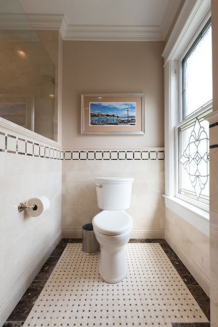 Bathroom with toilet, art, and window, featuring black and white accents and neutral tones.
