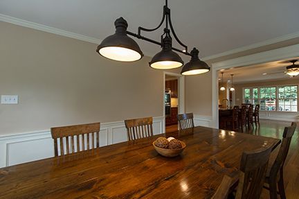 Dining room with wooden table, chairs, and pendant lights; doorway to another room.