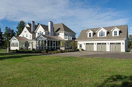 Large white house with attached garage; green lawn, blue sky.
