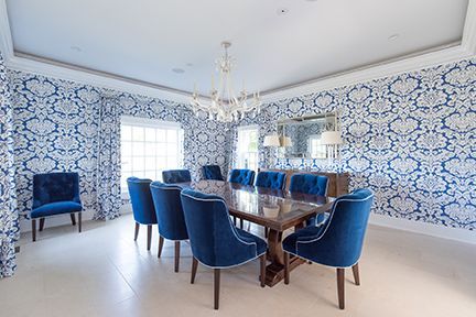 Elegant dining room with blue patterned wallpaper, blue velvet chairs, and a wooden table.