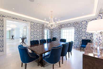 Elegant dining room with blue velvet chairs, patterned wallpaper, chandelier, and a table set for a gathering.