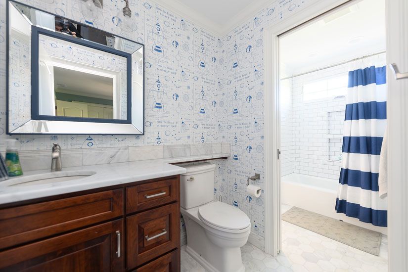 Bathroom with blue patterned wallpaper, a dark wood vanity, and a white and blue striped shower curtain.