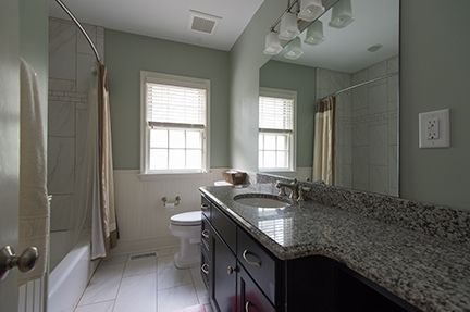 Bathroom with light green walls, dark vanity, granite countertop, and a white toilet.