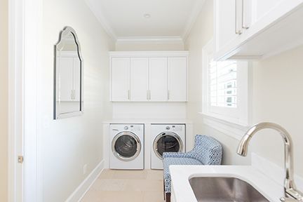White laundry room with washer, dryer, cabinets, sink, chair, and mirror.