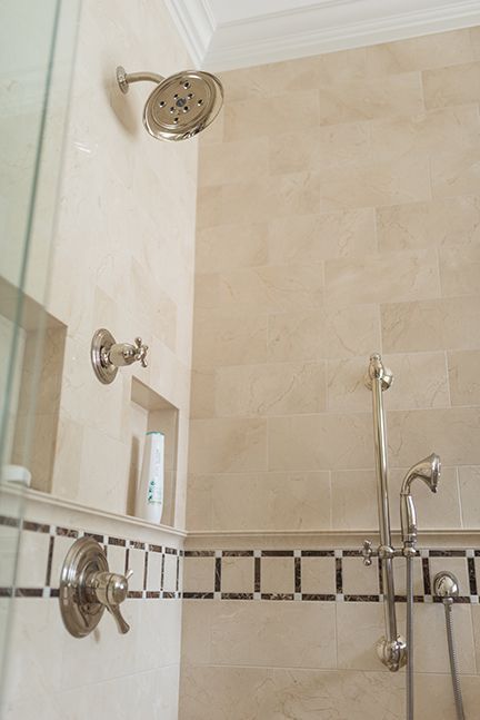 Shower interior with beige tile, chrome fixtures, and a hand shower head.