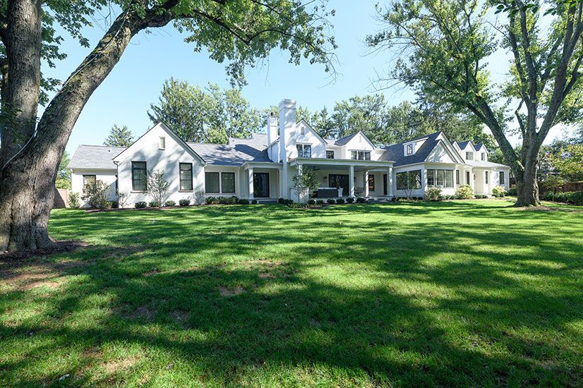 White house with black windows and a large green lawn under trees.