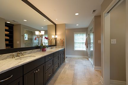 Modern bathroom with double vanity, large mirror, and walk-in closet. Beige and dark brown tones.