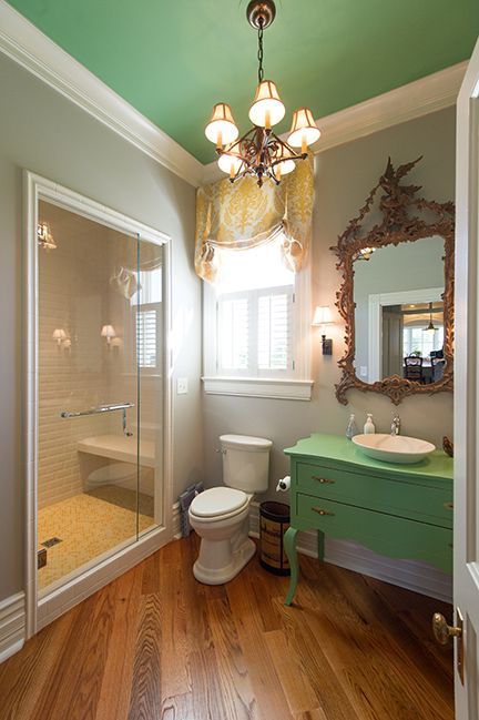 Bathroom with a green ceiling, vanity, and hardwood floors; a glass shower, toilet, and ornate mirror are also present.