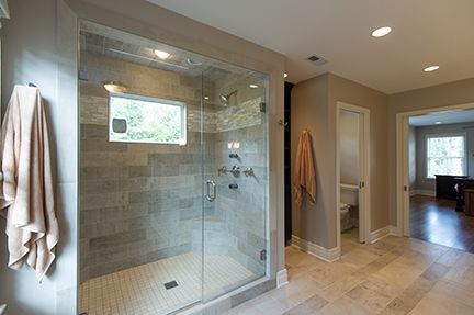 Modern bathroom with glass shower, gray tile, beige walls, and a towel.
