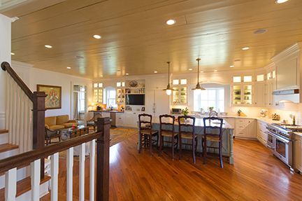Open-concept kitchen with island and seating, leading to living area. Hardwood floors, white cabinets, neutral walls.