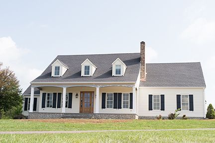 White house with black shutters and a porch, blue sky.