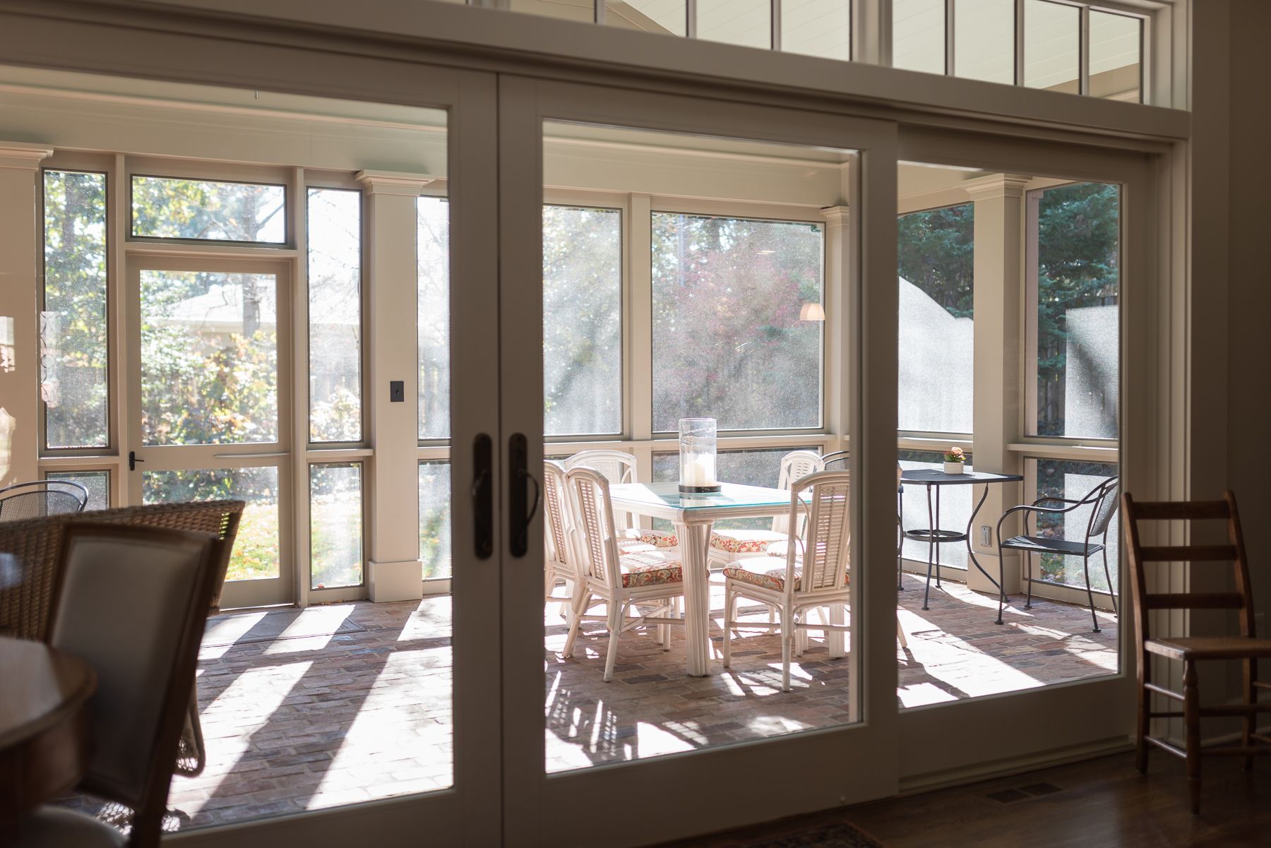 Sliding glass doors open to a screened porch with a table and chairs, sunlight streaming in.