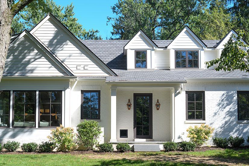 White house with black-framed windows and a dark door, set on a lawn with bushes and trees.