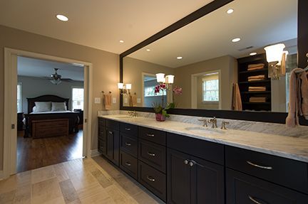 Bathroom with dark cabinets, long mirror, and doorway to a bedroom.