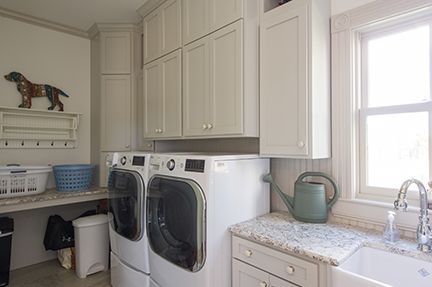 Laundry room with white washer/dryer, light gray cabinets, sink, and window.