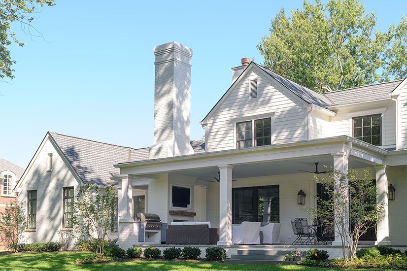 White house with a porch, chimney, and windows, on a sunny day.
