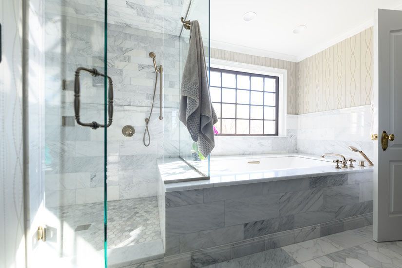 Marble bathroom with glass shower, soaking tub, window, and gray towel.