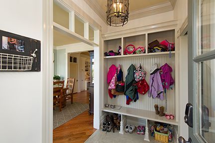 Entryway with built-in storage: coats, shoes, hats, and a chalkboard. White walls, wooden floors, and a hanging light fixture.