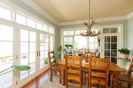 Dining room with wooden table, chairs, and a chandelier, surrounded by large windows.