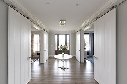 A bright hallway with white sliding doors, a round table with flowers, and a dark front door.