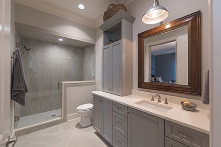 Bathroom with shower, toilet, vanity with a mirror, and storage cabinets in a modern, light gray and white design.