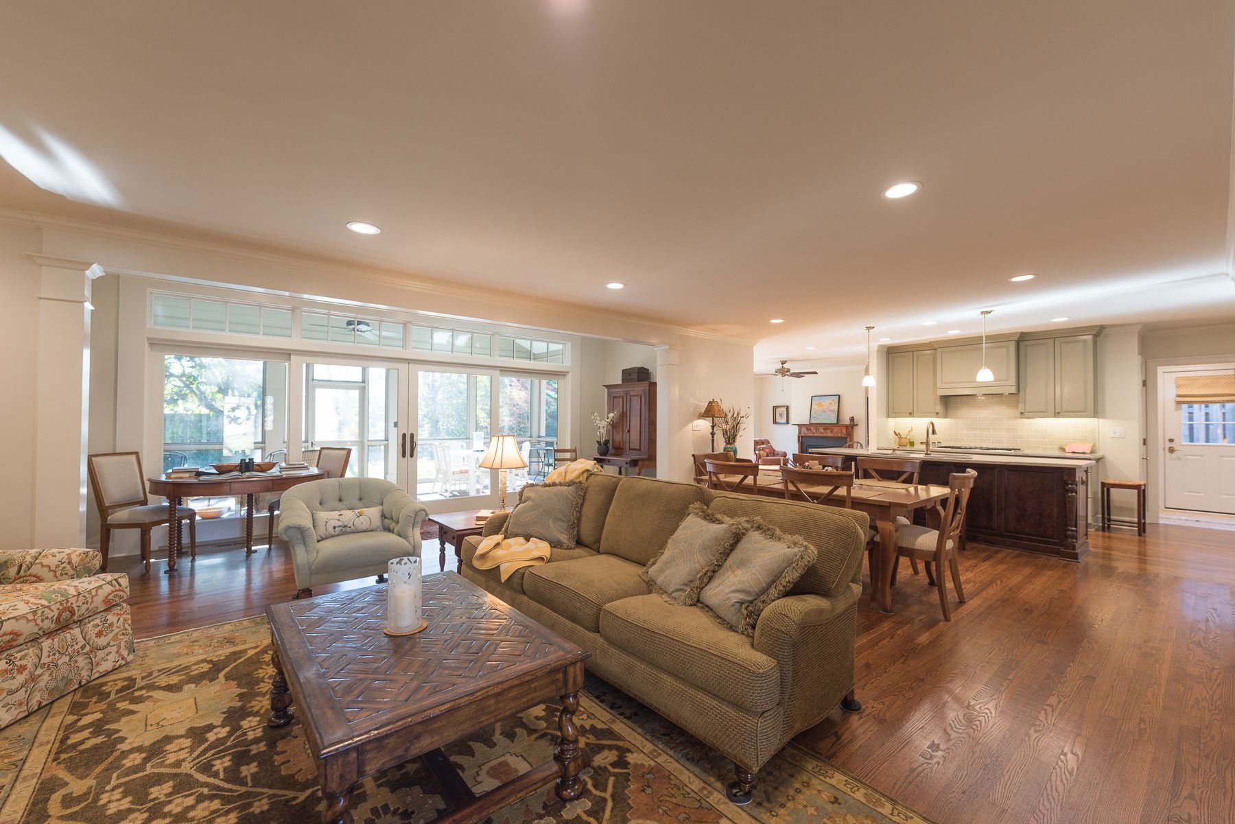 Spacious living room with open layout. Brown sofa, rug, and wooden floors. Kitchen and dining area visible.