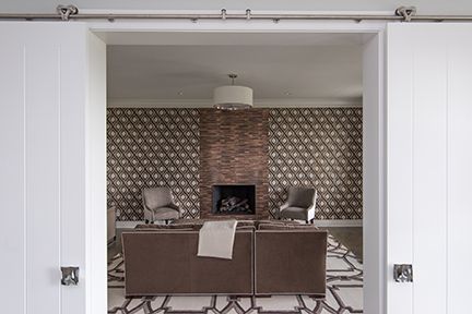 White sliding doors open to a living room with a fireplace, patterned wallpaper, and modern furniture.