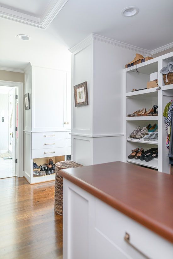 Walk-in closet with white shelves and drawers, brown countertop and wooden floor.