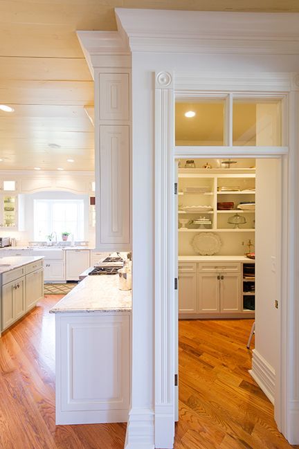 White kitchen with pantry. White cabinets, marble countertop, wooden floors, and an open doorway.