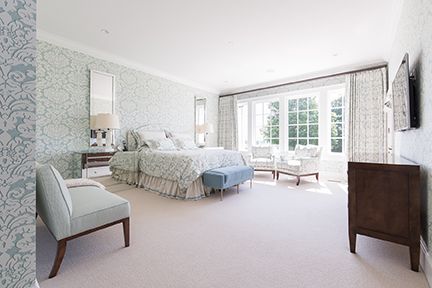 Elegant bedroom with light blue floral wallpaper, a large window, and soft-colored furniture.