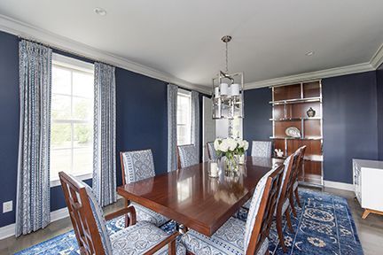 Formal dining room with navy blue walls, a wooden table, and patterned chairs.
