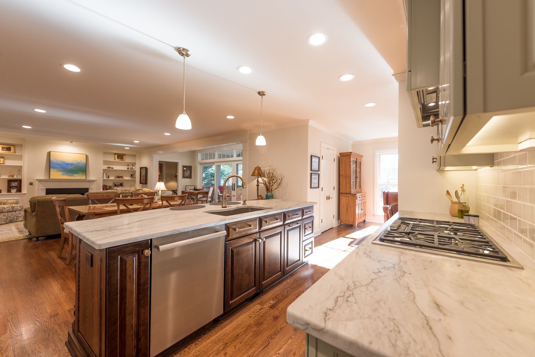 Open-concept kitchen with island, dark wood cabinets, and light countertops, leading to a living area with a fireplace.
