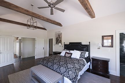 Spacious bedroom with vaulted ceiling, dark wood beams, and a black and white patterned bedspread.