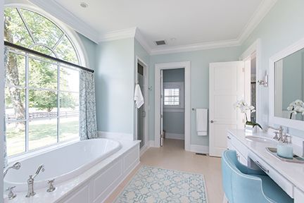 Spacious blue and white bathroom with a large arched window, bathtub, and vanity.