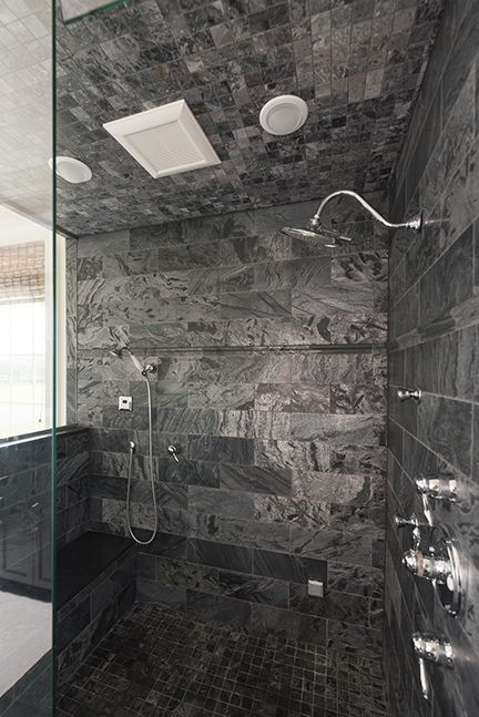 Dark gray tiled shower with rain showerhead and multiple chrome fixtures.