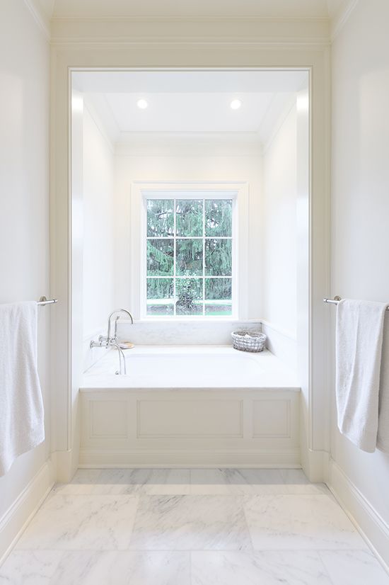 Bright white bathroom with built-in bathtub under a window, flanked by towel racks.