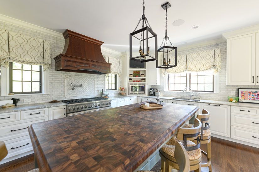 White kitchen with a large butcher block island, wooden hood, and pendant lights.