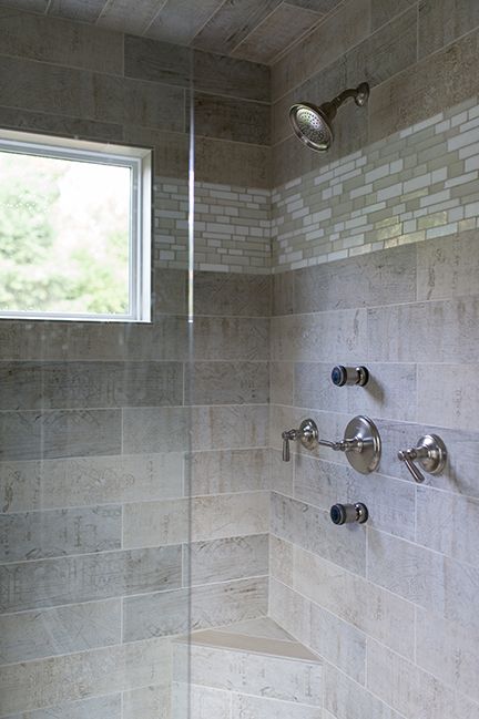 Shower with gray tile, glass door, and chrome fixtures. A window offers natural light.