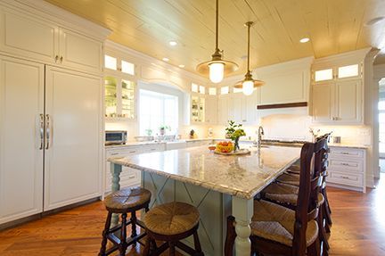 Bright kitchen with white cabinets, wooden island, and stools; two hanging lights over the island.